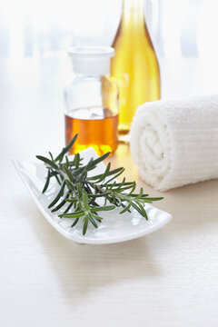 Sprig of rosemary and a towel with bottles of aromatic oil for aromatherapy