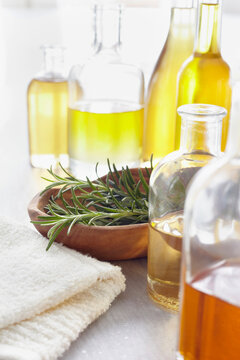 Sprig of rosemary in a bowl, fresh herbs, a towel and bottles of essential oil for aromatherapy