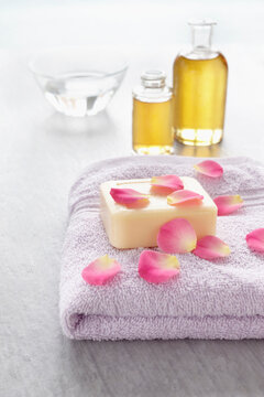 Rose petals and bath products like towel, soap and bottles of essential oil for aromatherapy and wellness
