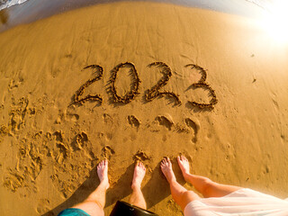 2023 written in sand and feet of a couple New Year on the beach