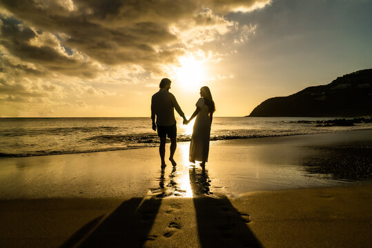 silhouette of young engaged couple holding hands in love during the sunset on a sandy island beach