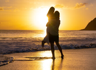 Silhouette of man picking up woman during the golden hour sunset on a island beach