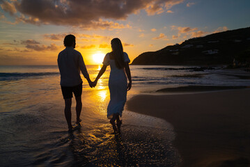 Young romantic dressed up couple walking down island beach towards the picturesque sunset