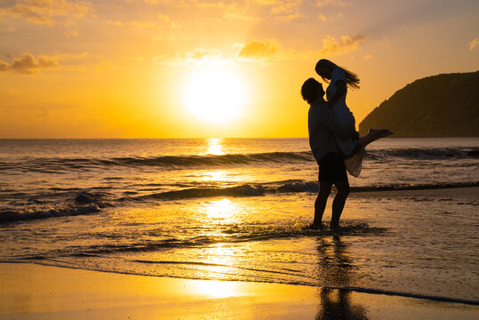 Silhouette of man picking up woman during the golden hour sunset on a island beach