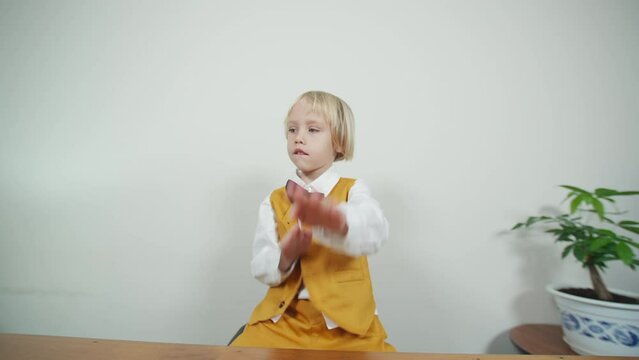 Funny cute 5 years old boy in yellow suit and black tie-bow plays imaginary musical instrument and dances. Playful caucasian boy pretends playing piano emotionally