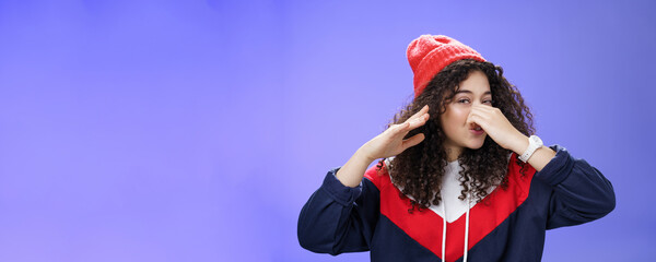 Gosh what stink. Portrait of cute caucasian girl with curly hair in cute trendy hat close nose with...