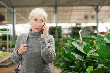 Senior European woman talking on phone while shopping in floral store.