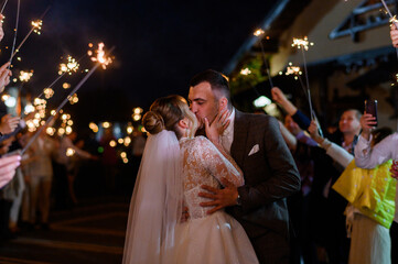 Side view of beautiful bride and bridegroom, which hugging and kissing each other while guests...
