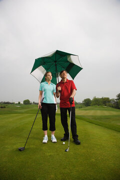 Father and Daughter on the Golf Course Holding a Large Umbrella