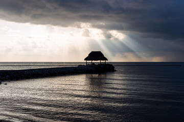 silhouette d'une cabane avec un toit de paille sur la mer avec des rayons de soleil à travers les nuages