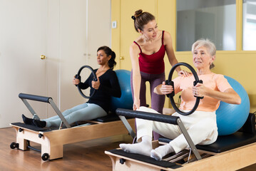 Two active women practicing Pilates in training perform an exercise using special rings and a fitball, where a female ..instructor helps to do it correctly