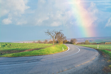 Rainbow. Empty road in the countryside. dry asphalt. Good weather - 555759901