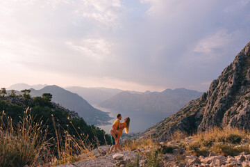 A couple of tourists are embraced standing on top of a mountain in Montenegro. - obrazy, fototapety, plakaty