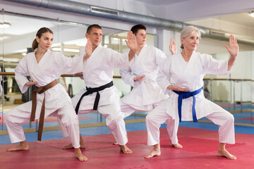 Concentrated people of different ages in kimonos practicing punches in gym during group martial arts workout. Shadow fight, combat sports training concept ..