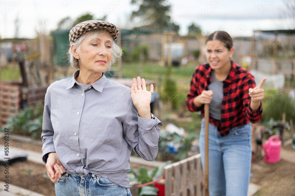 Wall mural two disappointed young and old female neighbors quarreling while digging garden during daytime in ap