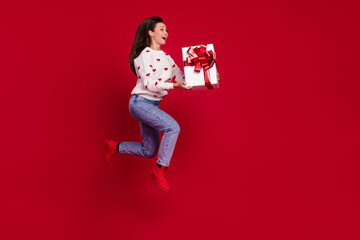 Full length photo of pretty cute lady wear white sweater holding gift jumping high running empty space isolated red color background