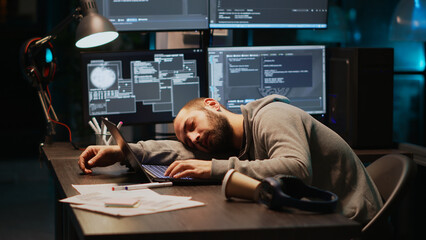Male programmer falling asleep on office desk, feeling tired and trying to work on database server....