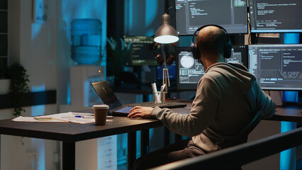 Software engineer typing programming code on laptop with multiple monitors, working with html...