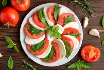 Italian caprese salad tomato basil mozzarella, in a plate on a wooden table