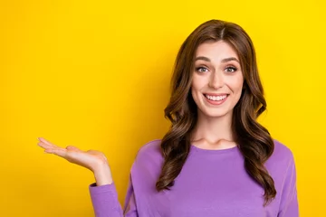 Fotobehang Photo of cute excited lady wear purple jumper wavy brown hair toothy beaming smile hold arm mockup promo isolated on bright yellow color background © deagreez