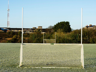 Irish sport training ground with tall goal posts for camogie, Gaelic football and rugby on a cold winter day. Frost on the green grass.