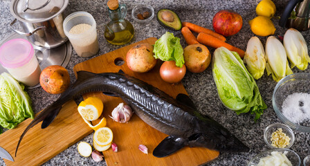 Fototapeta na wymiar Raw uncooked fish sturgeon at plate before preparing with vegetable on table.