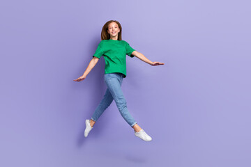 Fototapeta na wymiar Full length photo of shiny adorable small lady wear green t-shirt jumping high walking isolated violet color background