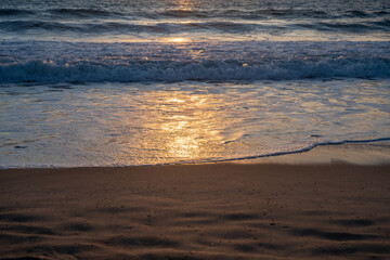 Sunset, sunlight reflected in the outgoing waves on the beach