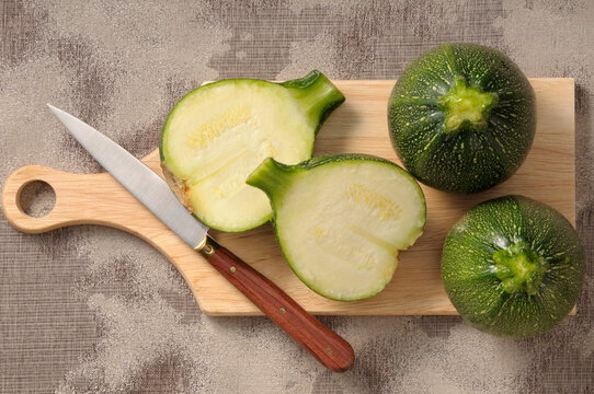 Overhead View of Round Zucchini on Cutting Board with Knife, One Cut in Half