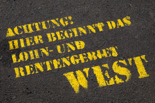Close-up of German text on paved road (Attention, Here begins the area of wage and pension West), Berlin, Germany