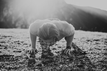 Muscular modern guy doing push-ups on top of mountain in nature