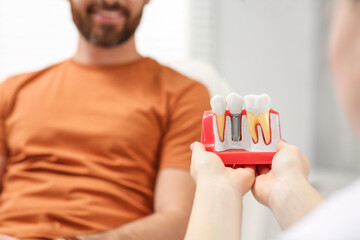 Doctor with educational model of dental implant consulting patient in clinic, closeup. Space for text