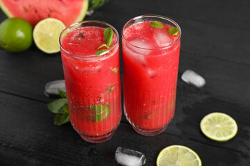 Glasses of delicious fresh watermelon juice, lime, mint and ice on black wooden table