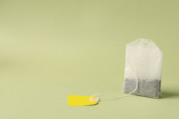 Paper tea bag with tag on light green background, space for text