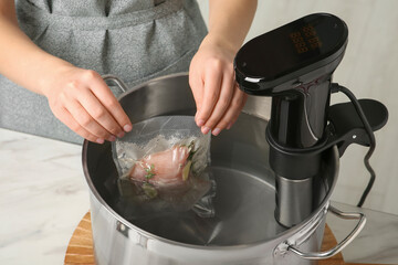 Woman putting vacuum packed meat into pot in kitchen, closeup. Thermal immersion circulator for sous vide cooking