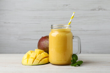 Mason jar with delicious fruit smoothie and fresh mango on white wooden table