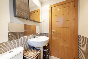 Fototapeta na wymiar Bathroom with rattan mesh furniture, wooden cabinet with mirror door, deep design porcelain sink and pear wood door