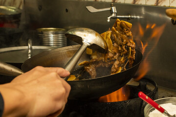 An asian chef stir frying beef with mushrooms with a saucepan and wok on fire