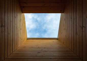 Dormer window in a wooden sloping ceiling overlooking blue sky. Sunlight enters the room through a window. Mansard roof