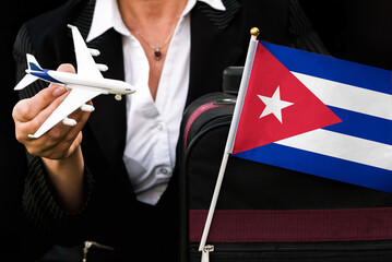 business woman holds toy plane travel bag and flag of Cuba
