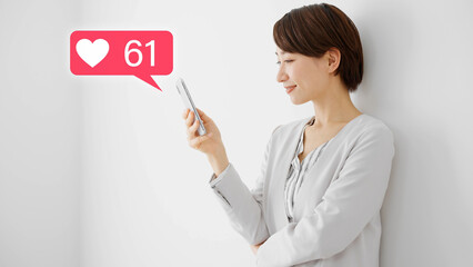 白い壁にもたれながらスマートフォンを操作する若い女性