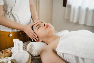 Pretty asian woman is given rejuvenating facial massage in an aroma room. Female therapist massaging the face and forehead of a relaxed client to a young woman. Alternative medicine.