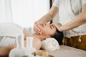 Pretty asian woman is given rejuvenating facial massage in an aroma room. Female therapist massaging the face and forehead of a relaxed client to a young woman. Alternative medicine.