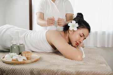 Obraz na płótnie Canvas Relaxed pretty asian young woman enjoying remedial body massage done by professional masseur in spa room, with herbal compress balls in therapy spa salon.