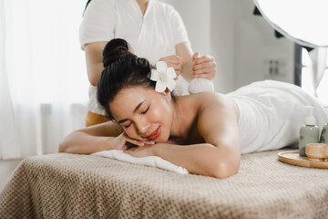Fototapeta na wymiar Relaxed pretty asian young woman enjoying remedial body massage done by professional masseur in spa room, with herbal compress balls in therapy spa salon.