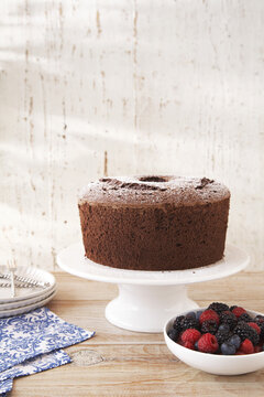 Chocolate cake with powdered sugar on a cake stand and a bowl of mixed berries to the side
