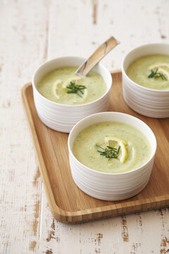 Green velvet soup topped with lemon and chives on wooden tray