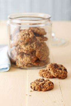 Oatmeal cookies in a glass cookie jar on a cream colored wood surface