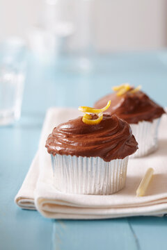 Chocolate frosted cupcakes with lemon zest and a candle on a blue background