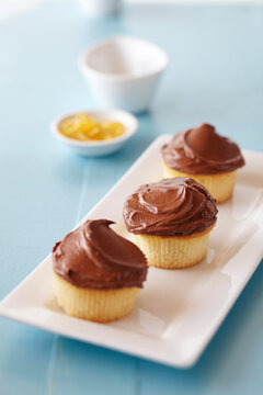 Chocolate frosted cupcakes on a blue background with small bowl of lemon zest in the background